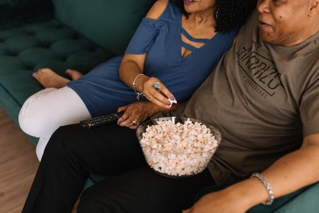 casal de homem e mulher negros assistindo ao amazon prime video com uma pipoca no colo