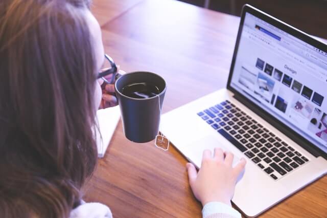 mulher segurando xícara com chá mexendo no notebook trabalhando em home office