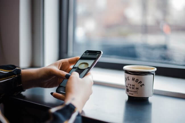 pessoa branca acessando aplicativo para editar video no celular com um café ao lado